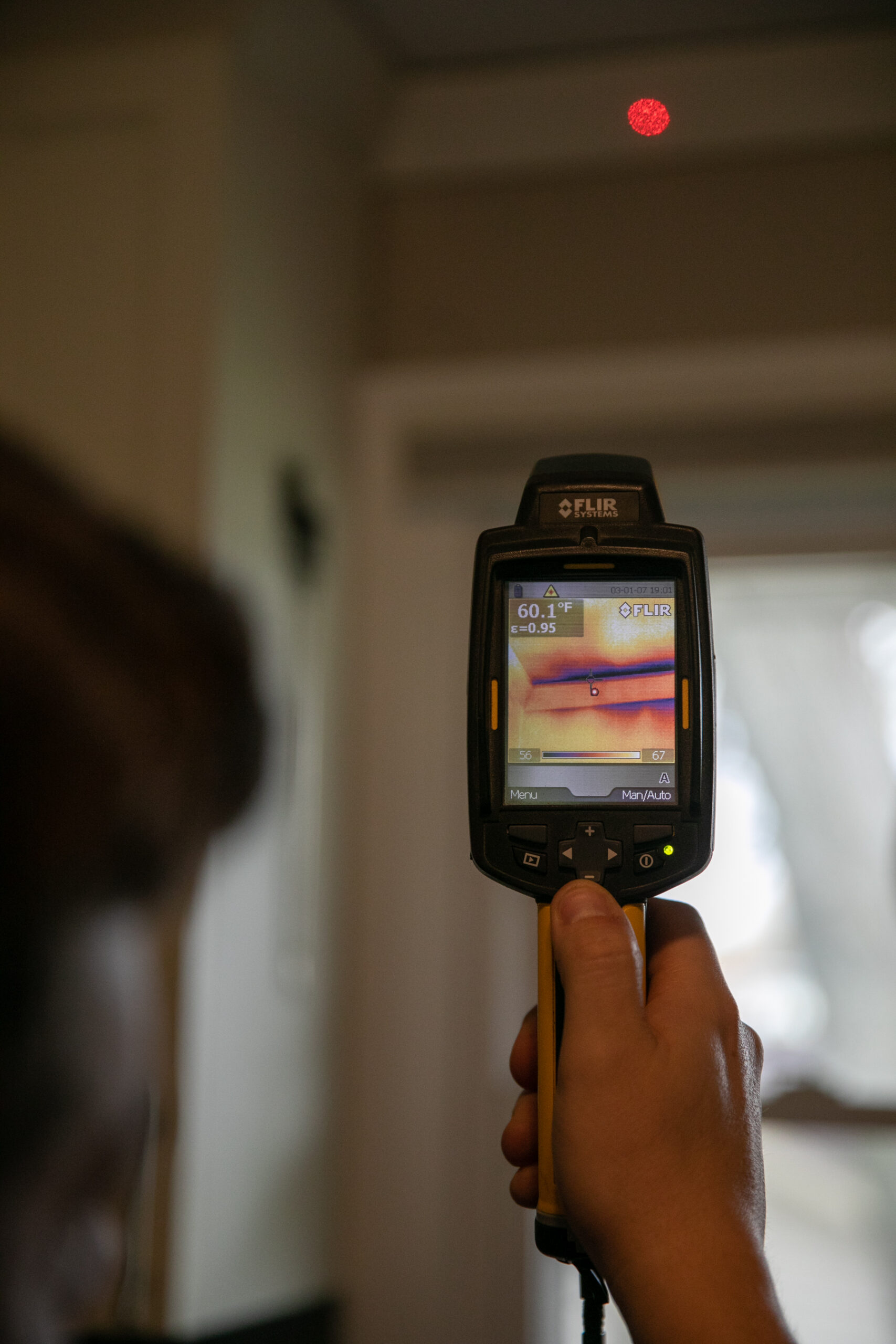 A person uses a FLIR thermal imaging camera to assess temperature differences, displaying a reading of 60.1°F on the screen.